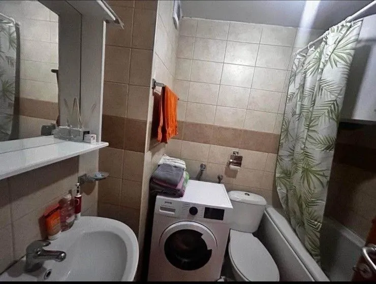 Jednostavno kupatilo sa veš mašinom, lavaboom i kadom sa zavjesom.