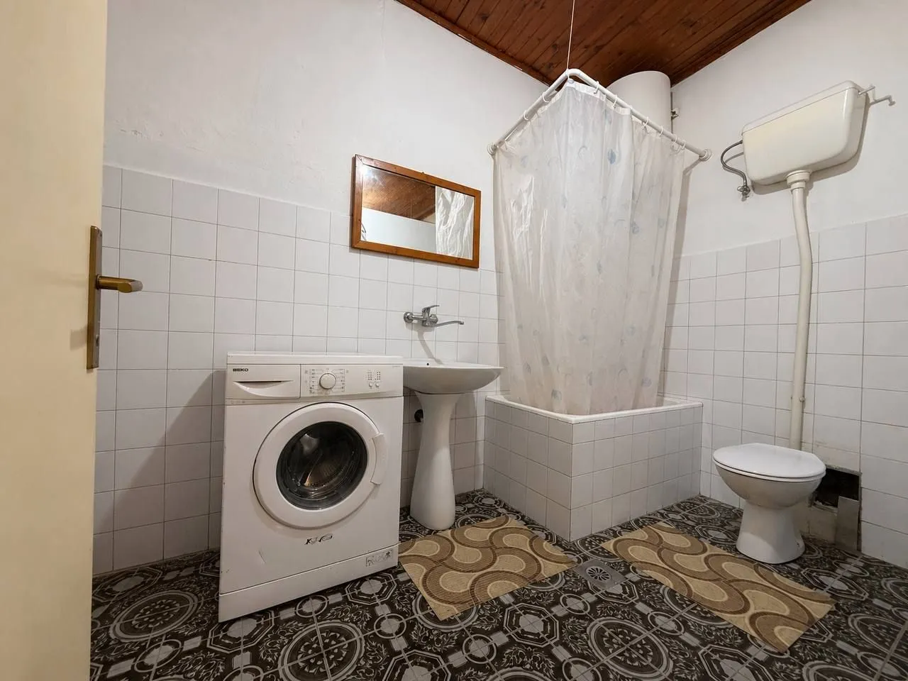 Starije opremljeno kupatilo sa kadom, umivaonikom i veš mašinom.