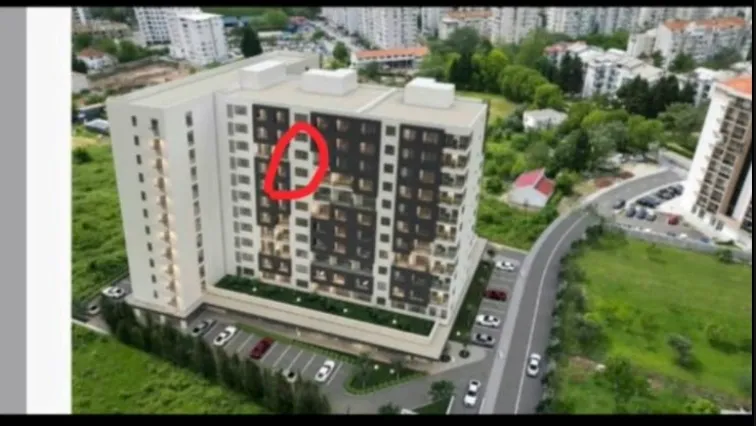 Pogled iz vazduha na višespratnu stambenu zgradu sa okolnim parkingom i zelenilom.