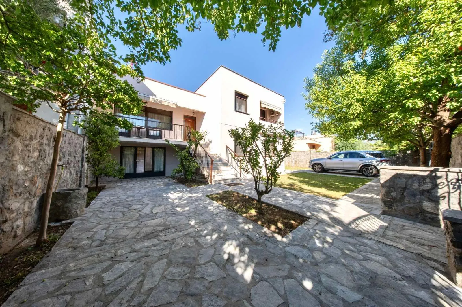Exterior of the house with a courtyard, paved area, and greenery.