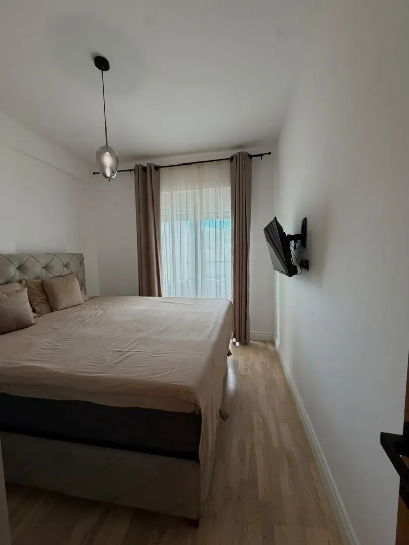 Furnished bedroom with a double bed, wooden flooring, and a wall-mounted TV.