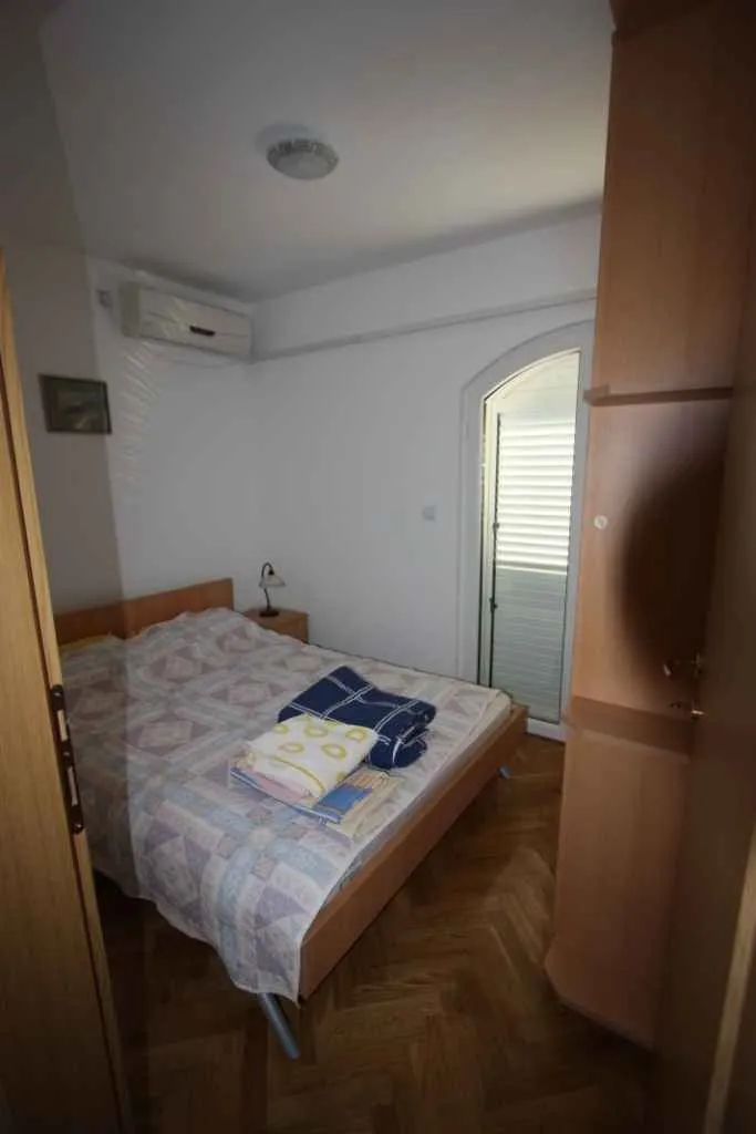 Manja spavaća soba sa bračnim krevetom, ormarom i izlazom na terasu.