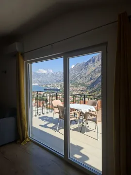 View through the balcony door to the terrace and the sea with mountains. - image 8