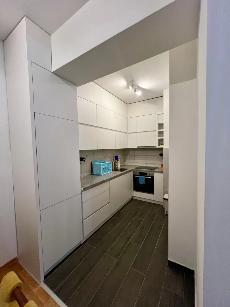 Modern white kitchen with built-in oven and dark floor.