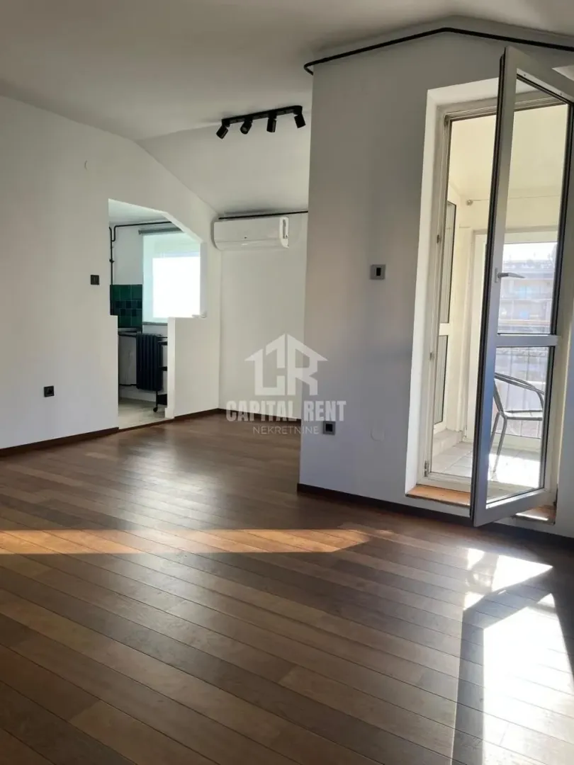 Empty living room with wooden flooring and access to the balcony.