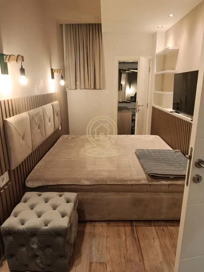 Modern bedroom with a double bed, upholstered headboard, and a wall-mounted TV.