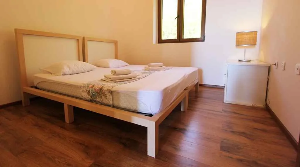 Svijetla spavaća soba sa dva spojena drvena kreveta i noćnim ormarićem.