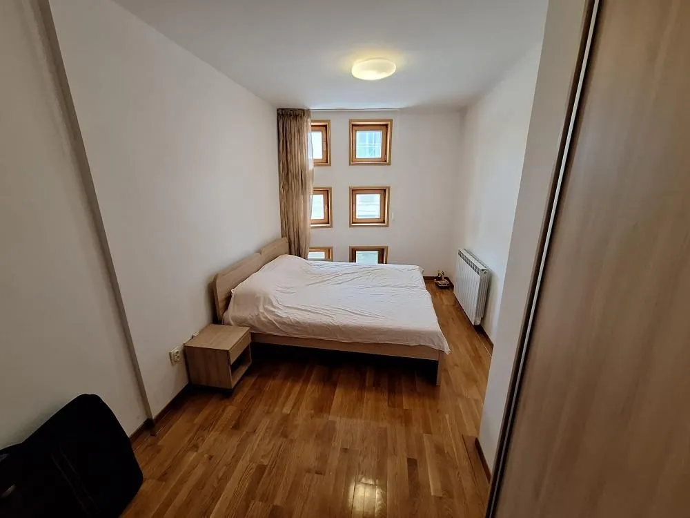 Spavaća soba sa bračnim krevetom, noćnim stočićem i prozorima.