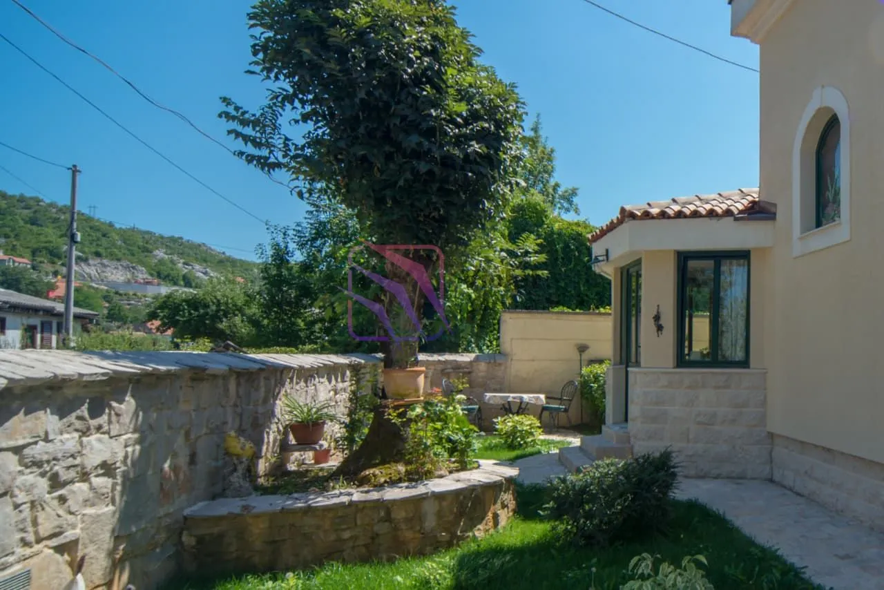 Pogled na dvorište i fasadu kuće sa kamenim zidom i zelenilom.