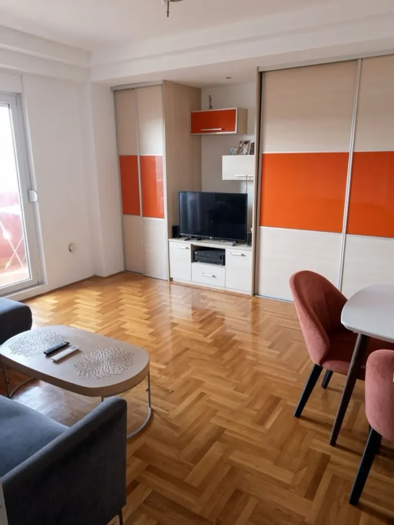 Dnevna soba sa garniturom, televizorom i trpezarijskim stolom.