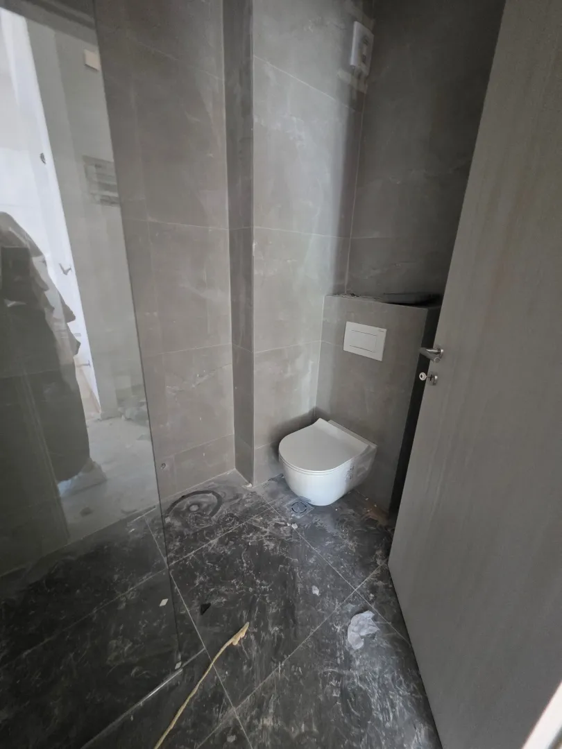Manje kupatilo obloženo sivim pločicama sa ugradnom šoljom.