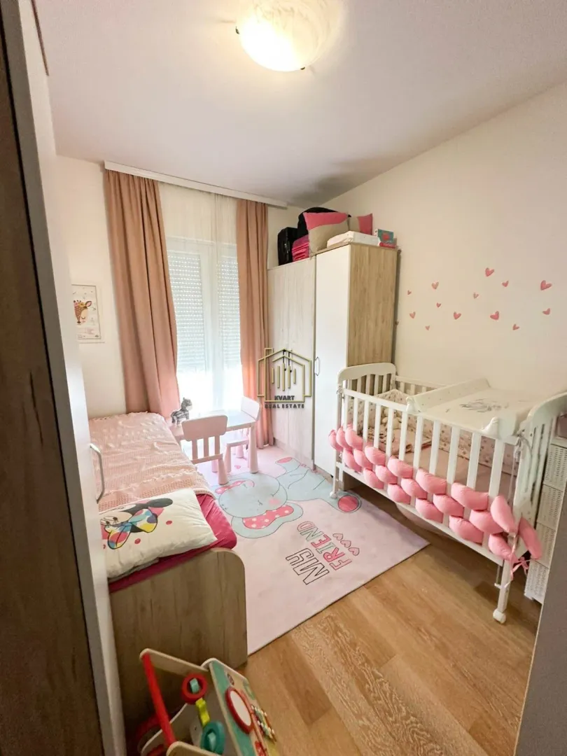 Dječja soba sa krevetcem, krevetom, ormarom i prozorom.