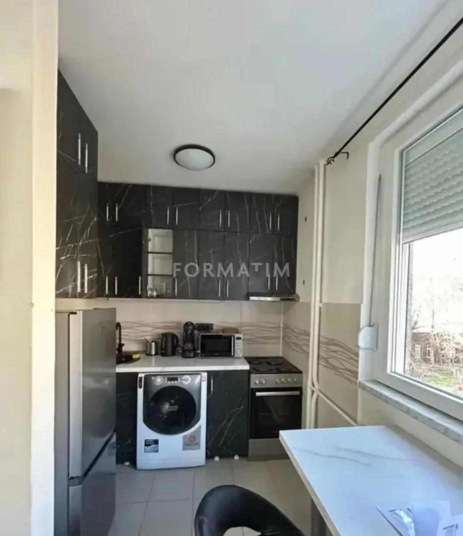 Manja kuhinja sa tamnim elementima, ugradnim aparatima i trpezarijskim stolom pored prozora.