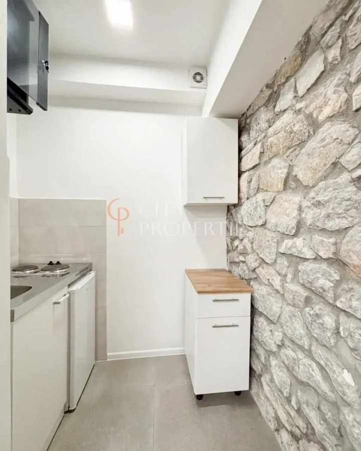 Small kitchen with white cabinets and a stone wall.