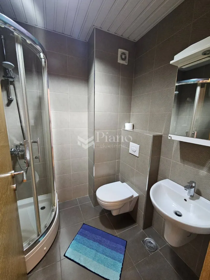 Compact bathroom with a shower cabin, washbasin, and toilet tiled in ceramic tiles.