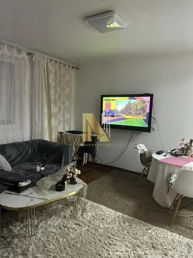 Dnevna soba sa garniturom, stočićem, televizorom na zidu i trpezarijskim delom.