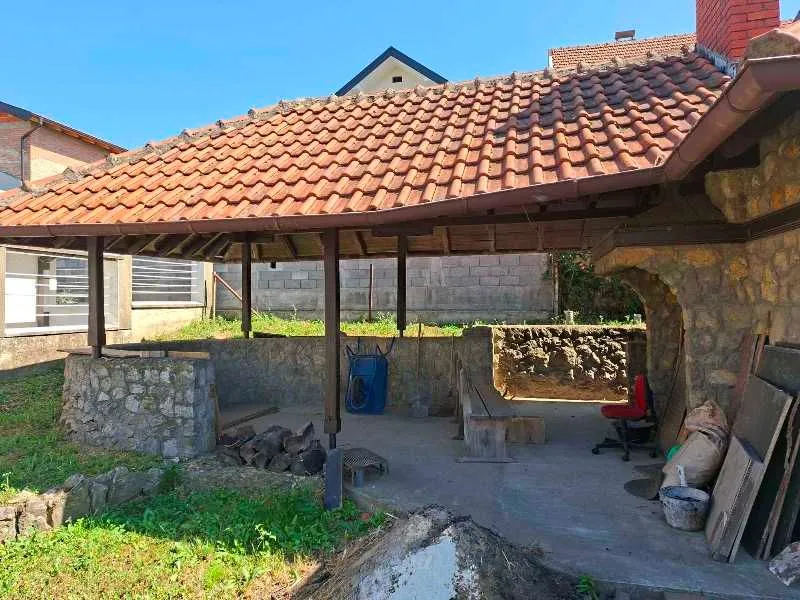 Natkriveni trem sa kamenim elementima i krovom od crepa u dvorištu kuće.
