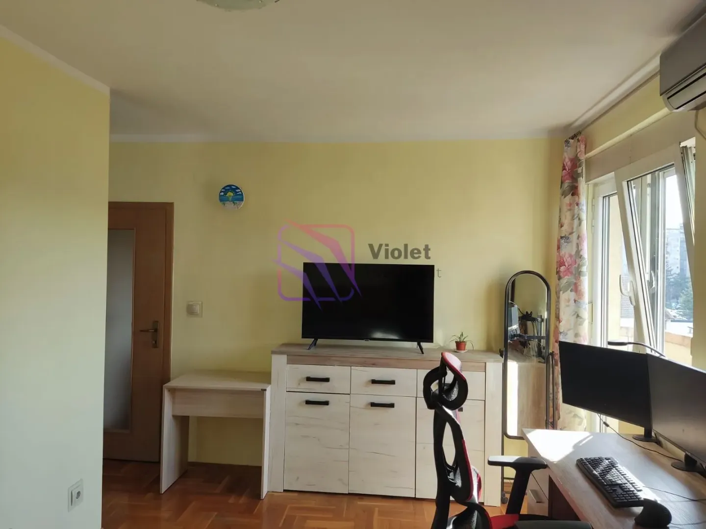 Dnevni boravak sa komodom za televizor, radnim stolom i izlazom na terasu.