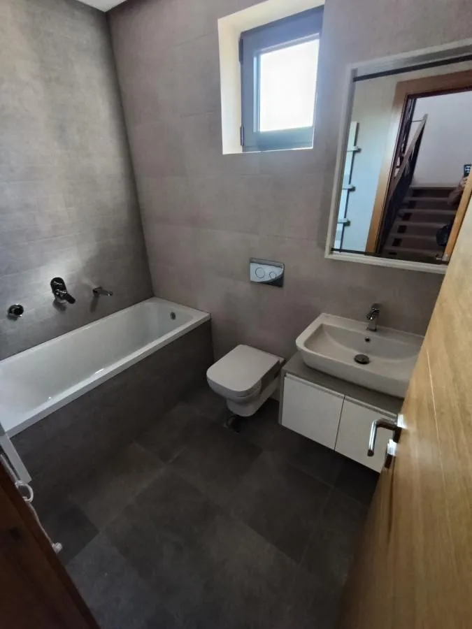 Modern bathroom equipped with a bathtub, washbasin, and toilet in grey tiles.