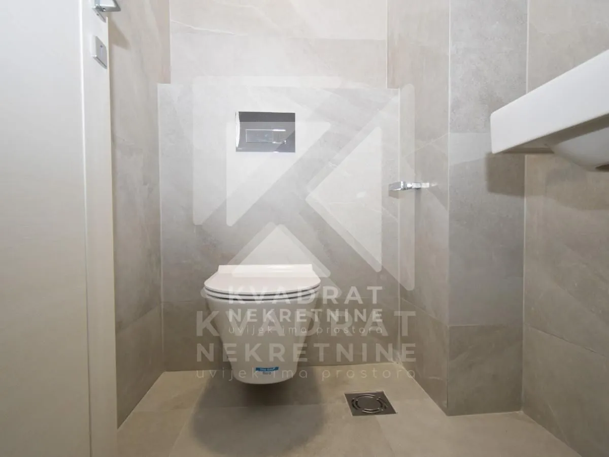 Modernly equipped bathroom with grey tiles and a wall-hung toilet.