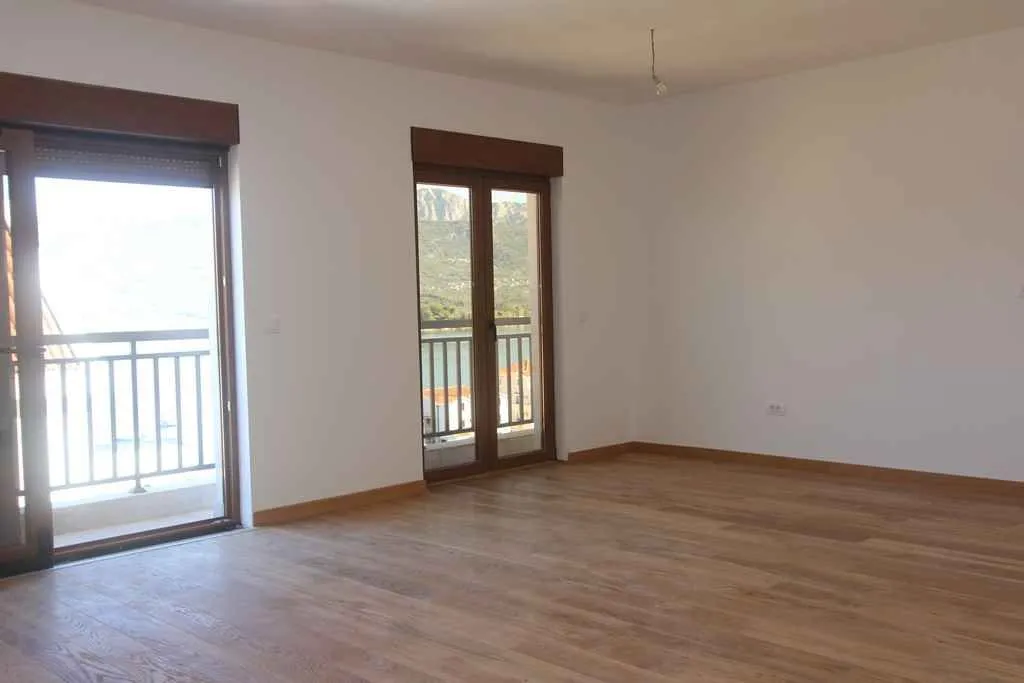 Prazna soba sa drvenim podom i izlazom na balkon.