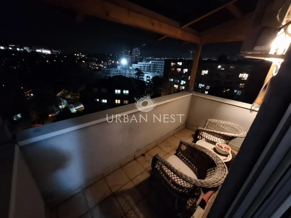Natkriveni balkon sa garniturom za sedenje i noćnim pogledom na grad.