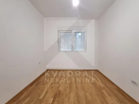 Prazna soba sa bijelim zidovima, drvenim parketom i prozorom. - image 6
