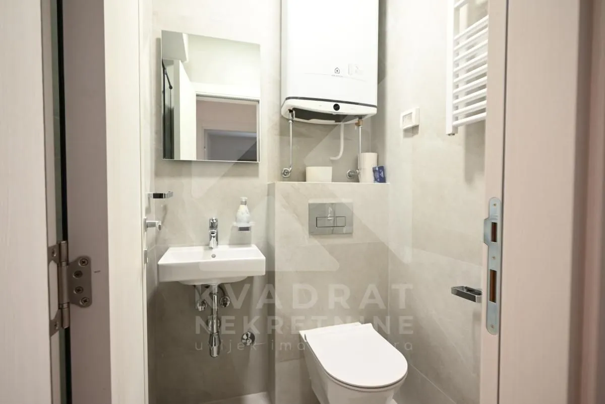 Small bathroom with a shower cabin, washbasin, toilet, and water heater.