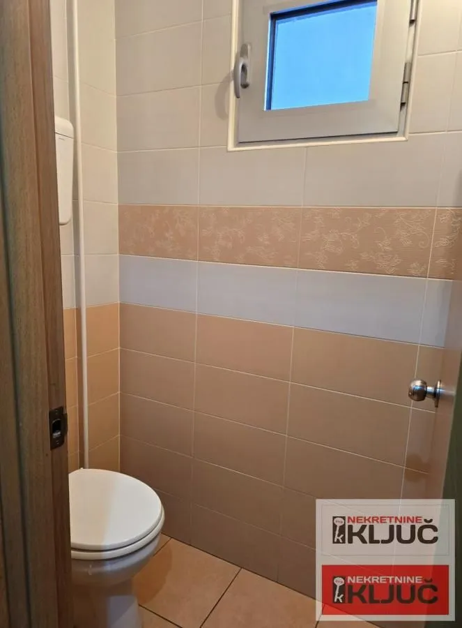 Small tiled bathroom with a toilet and a window.
