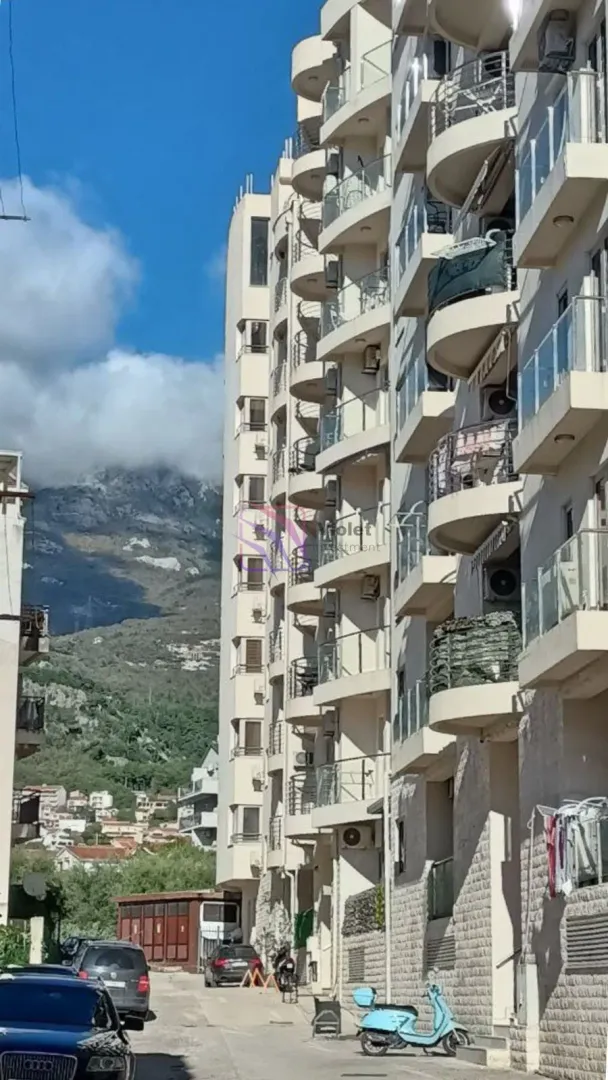 Pogled na spoljašnjost stambene zgrade sa terasam i planinskim pejzažom u pozadini.