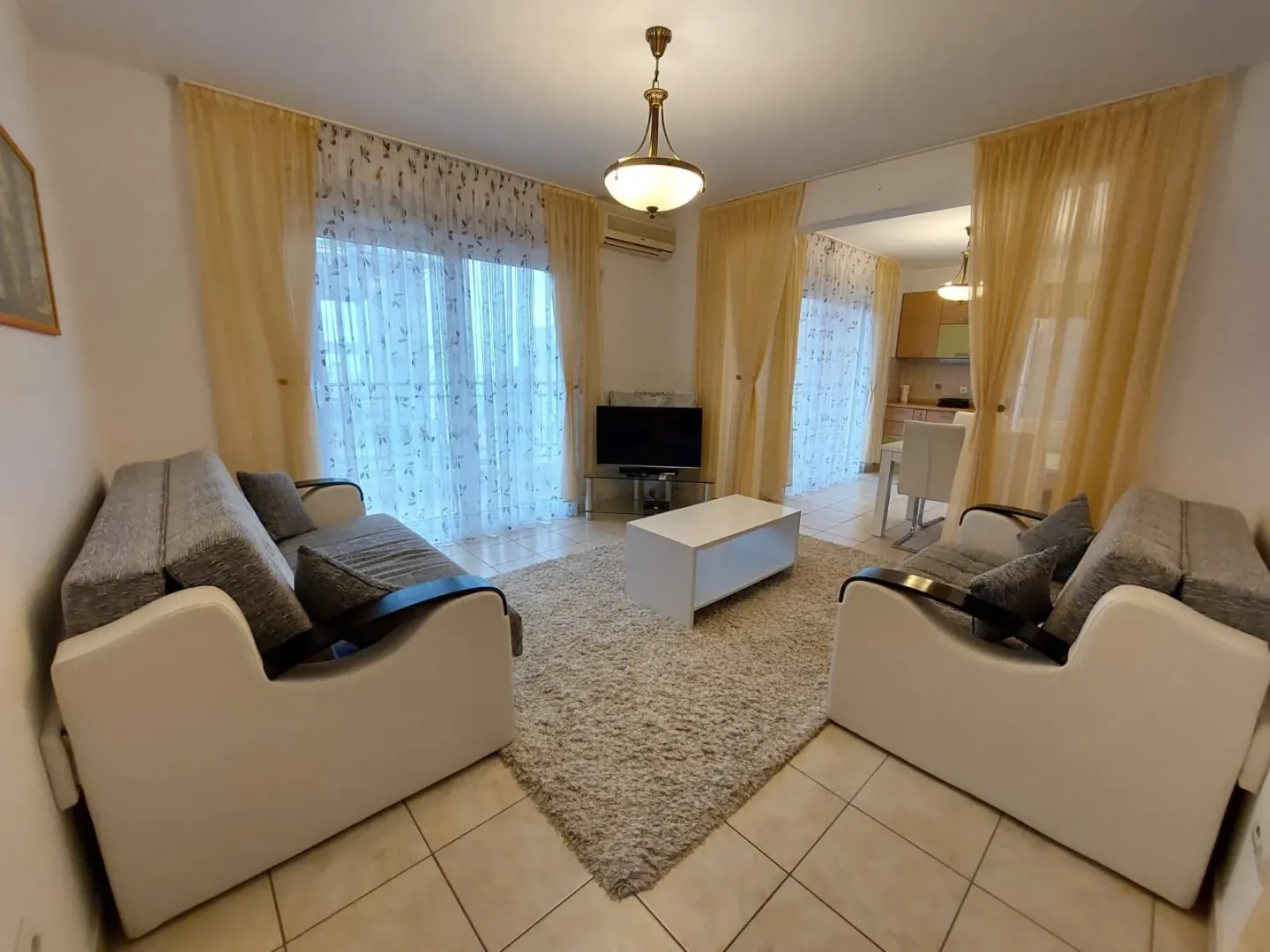 Dnevna soba sa garniturom, stočićem i televizorom, sa pogledom na trpezariju i kuhinju.