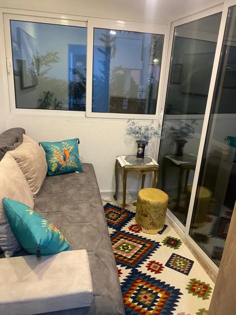 Enclosed balcony with seating furniture and a colorful rug.