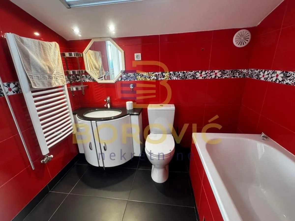Kupatilo sa crvenim zidnim pločicama, kadom, WC šoljom i umivaonikom.