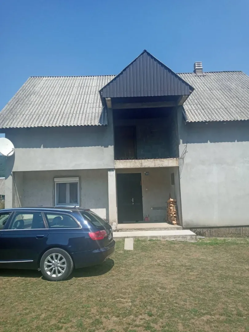Dvospratna kuća sa dvorištem i parkiranim automobilom.