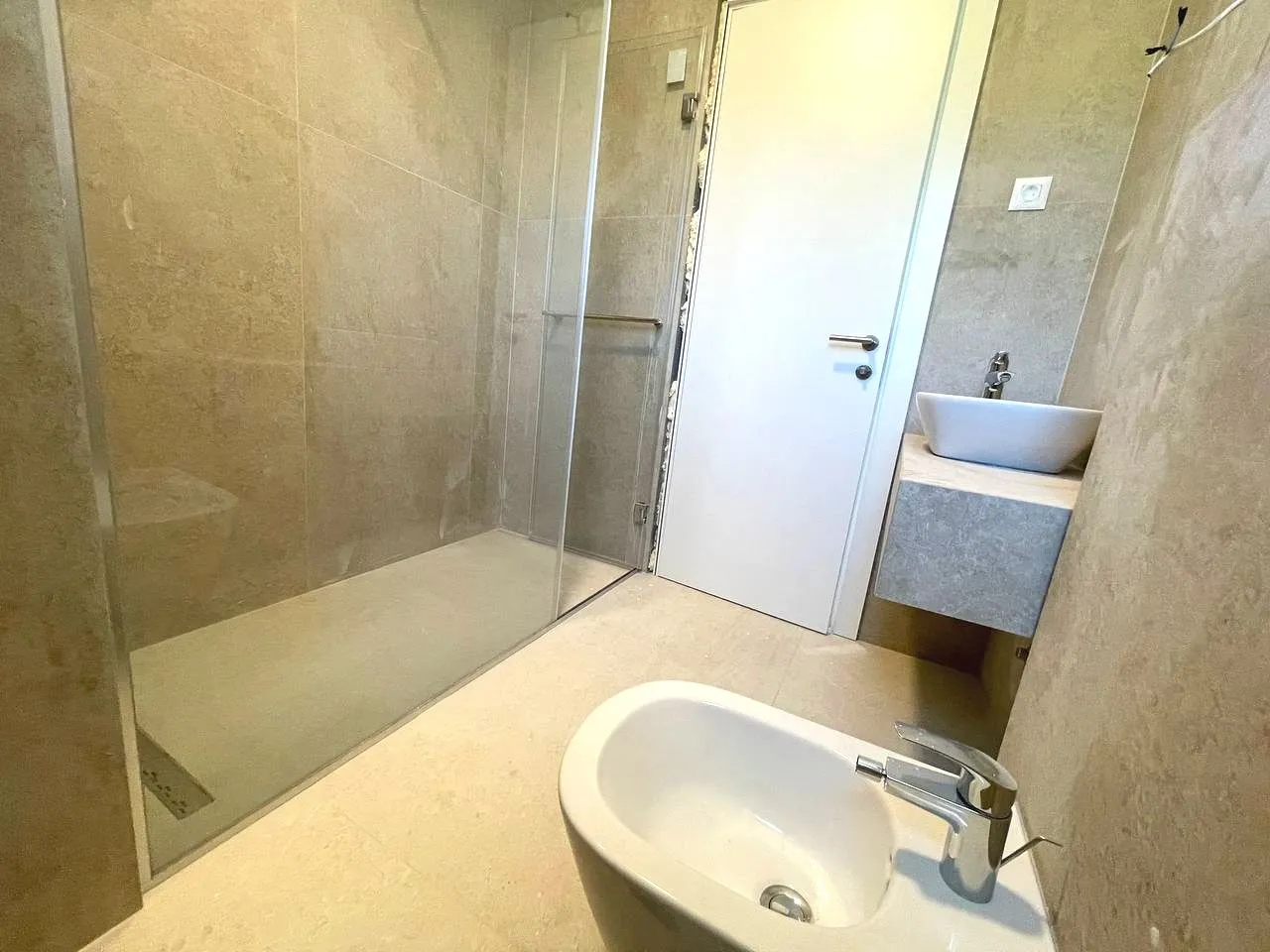 A modernly equipped bathroom with a walk-in shower, washbasin, and bidet.