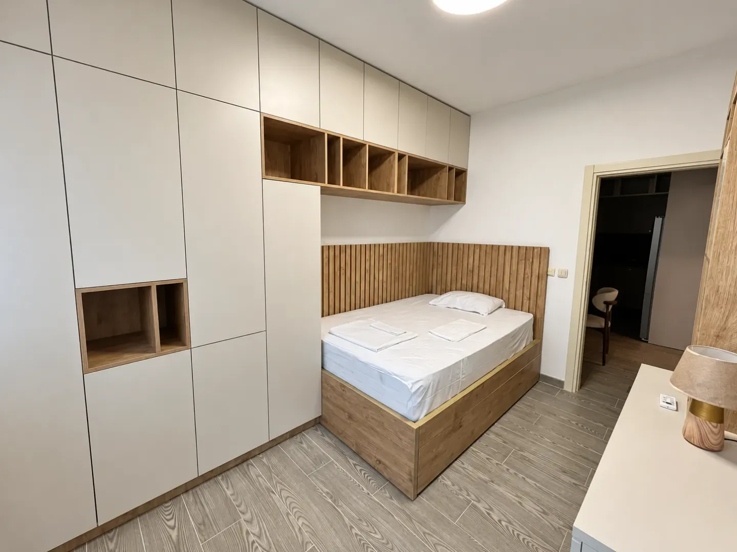 Modern bedroom with built-in wardrobes and a bed with a wooden headboard.
