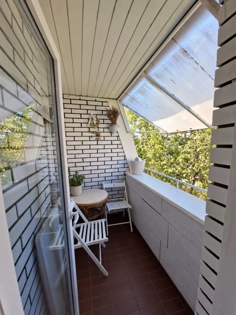 Covered balcony with seating furniture and a view of greenery.