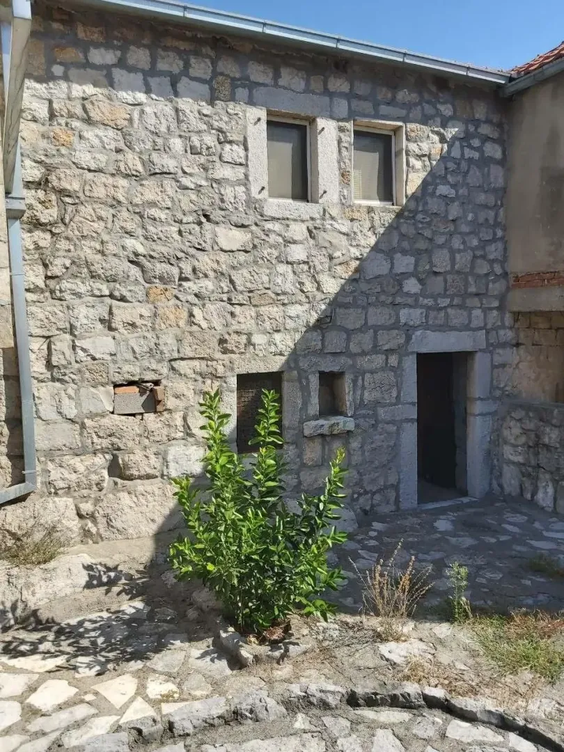 Kamena fasada stare kuće sa malim popločanim dvorištem.