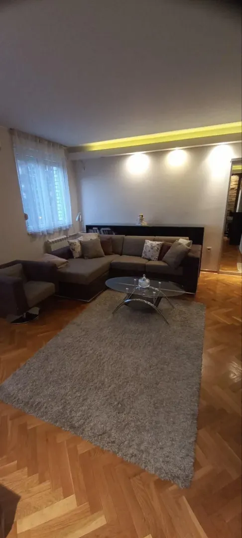 Dnevna soba sa ugaonom garniturom, staklenim stočićem i parketom.