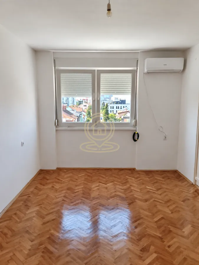 Prazna soba sa parketom na podu i prozorom sa pogledom na grad.