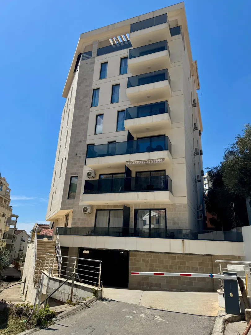 Exterior view of a modern multi-story building with balconies and ground-floor parking.