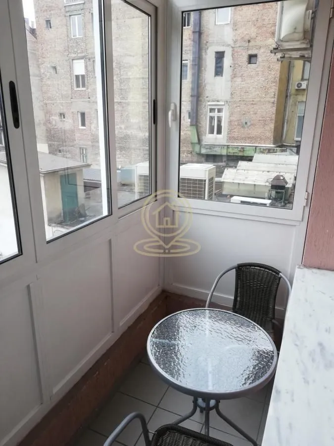 Zastakljeni balkon sa malim stolom i stolicama.