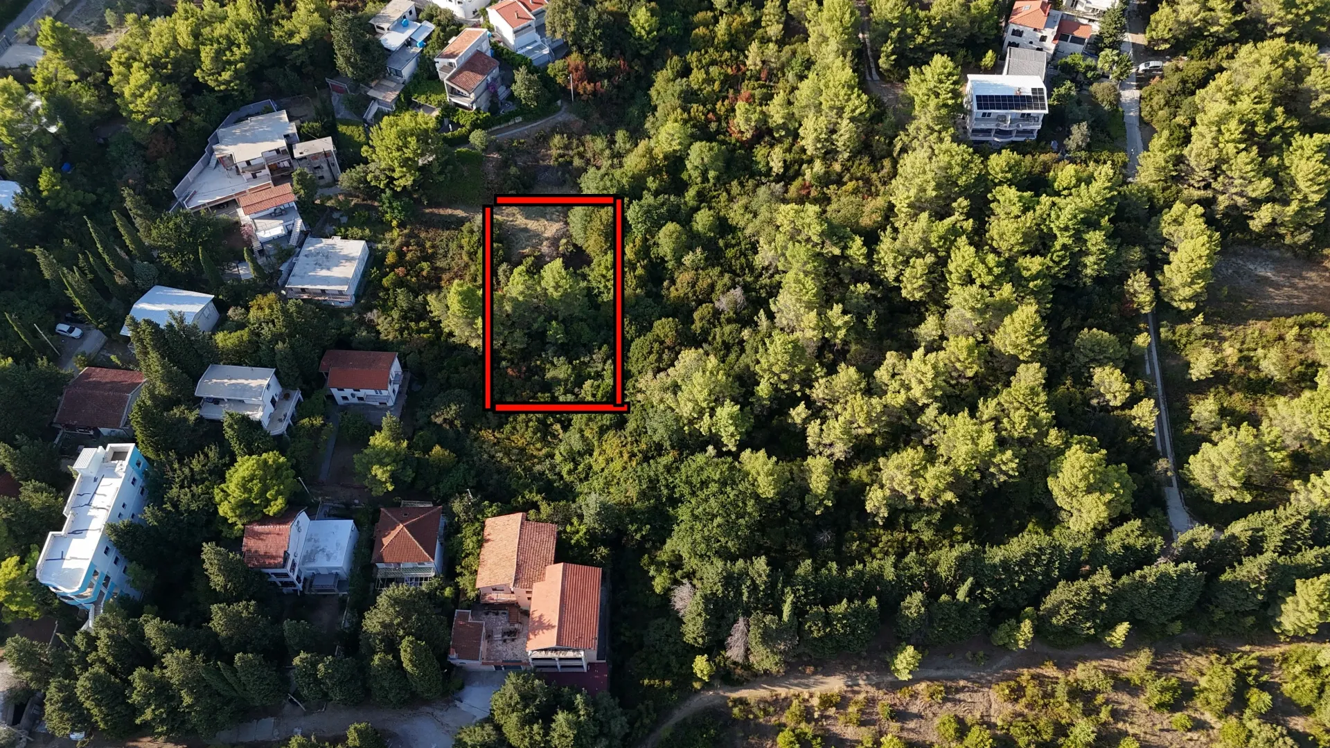 Pogled iz vazduha na građevinsku parcelu okruženu zelenilom.