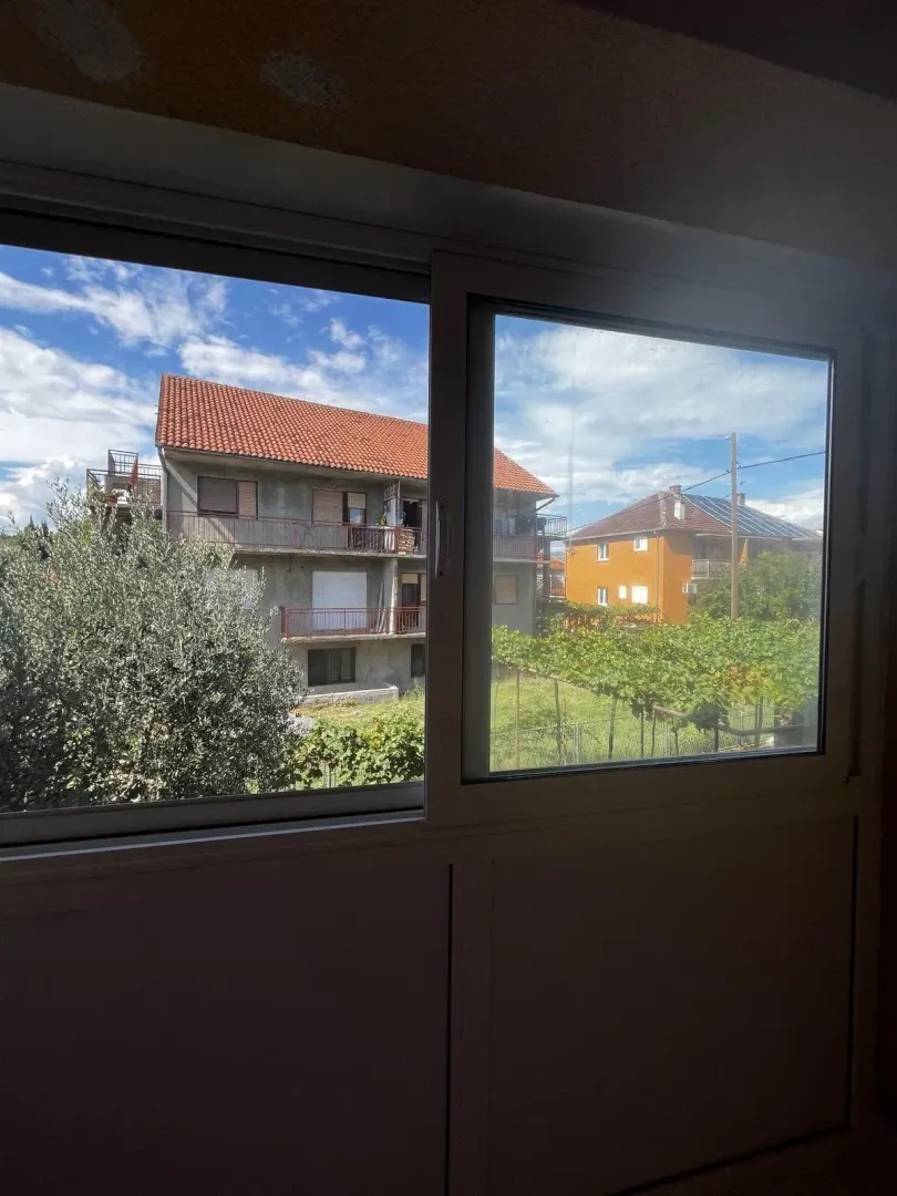 Pogled kroz prozor na okolne kuće i dvorište.