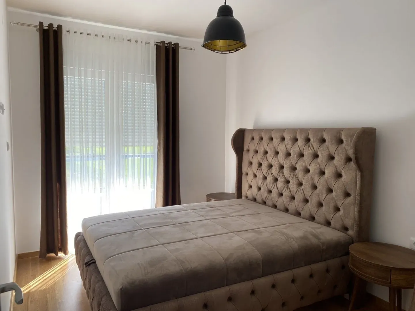 A bright bedroom featuring a large double bed with a tufted headboard.