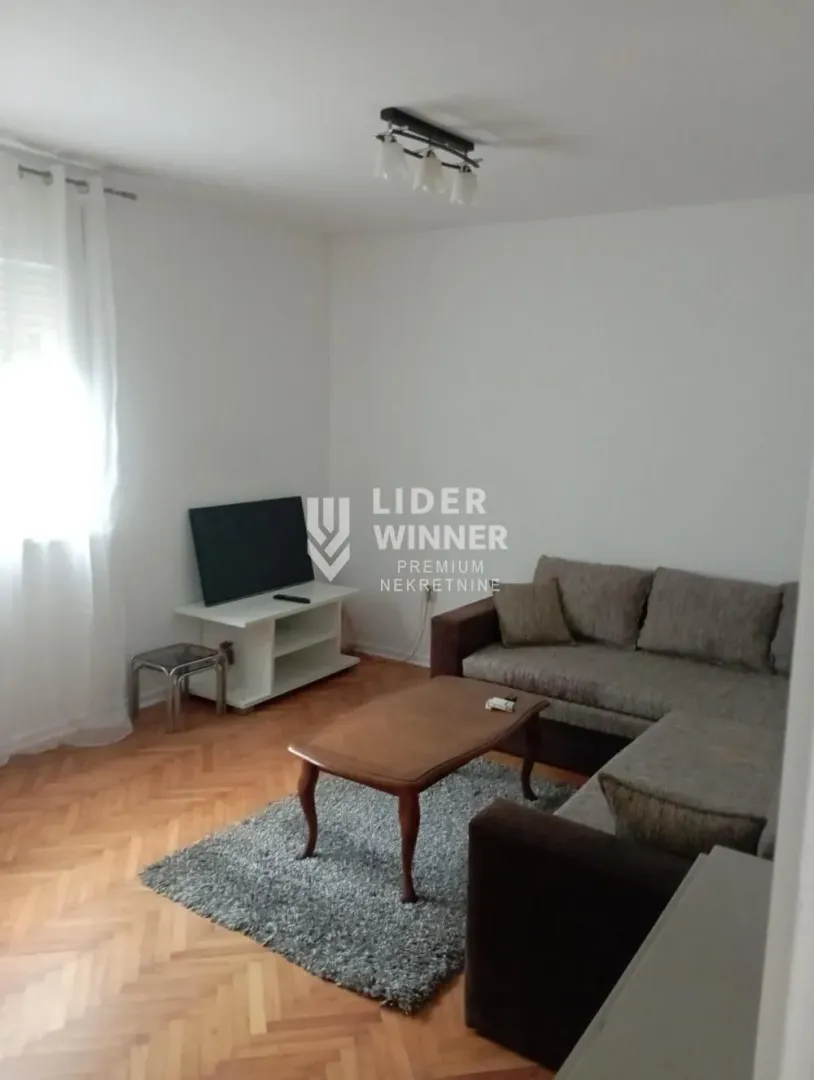 Dnevna soba sa garniturom, stočićem i TV-om.