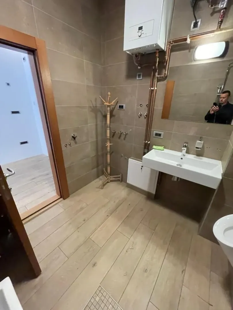 Kupatilo obloženo keramičkim pločicama sa umivaonikom i bojlerom na zidu.