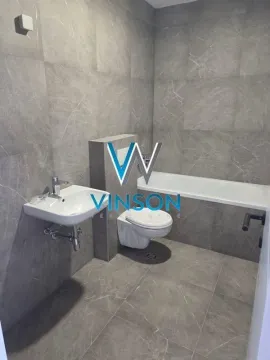 Modern bathroom lined with grey tiles featuring a bathtub, washbasin, and toilet. - image 3