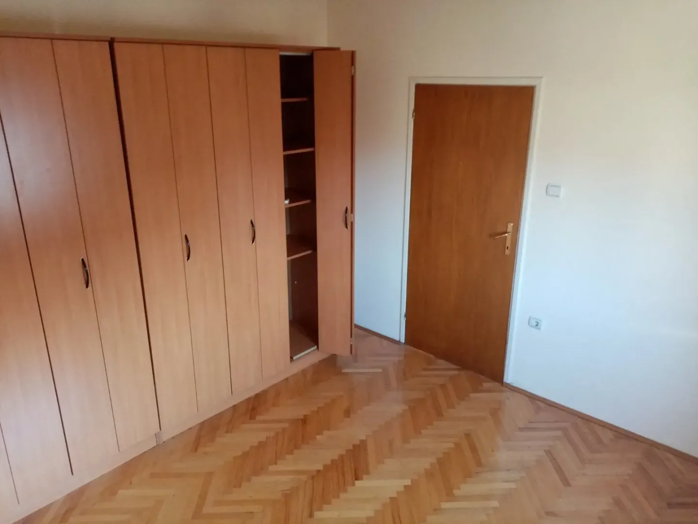 Bright empty room with a large wooden wardrobe and parquet flooring.