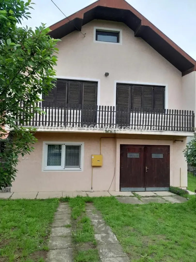 Prednji pogled na dvospratnu kuću sa balkonom i travnjakom u dvorištu.